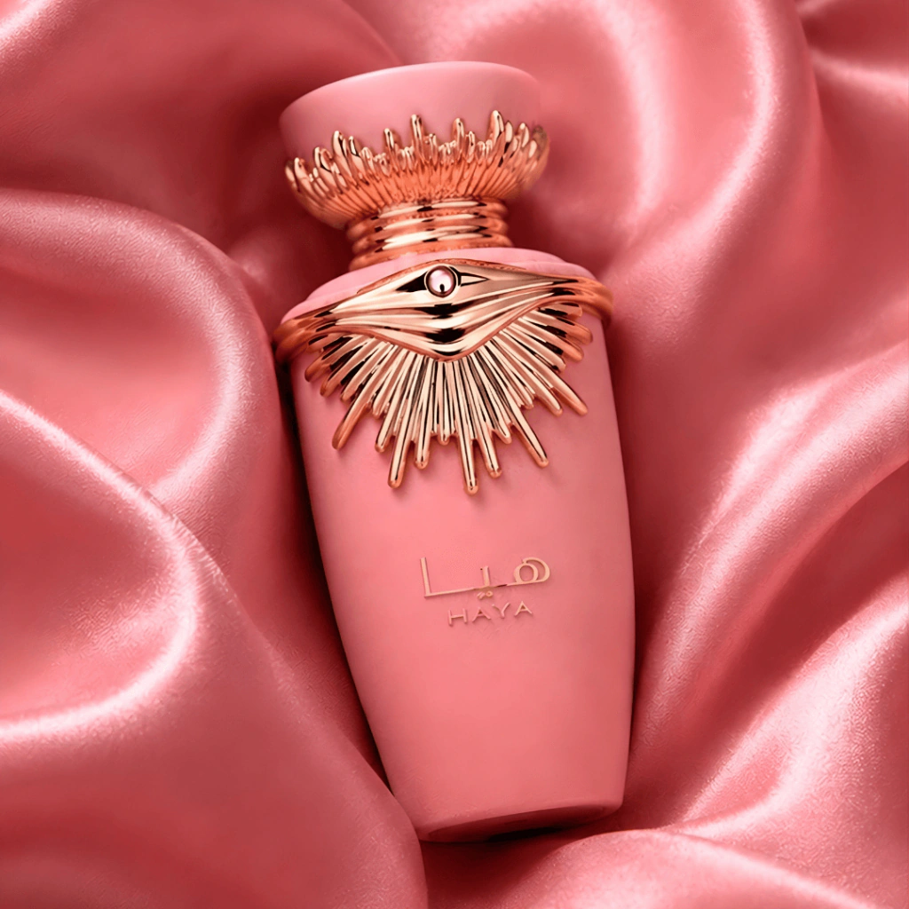 Frasco rosa do perfume Lattafa Haya, com coroa dourada, sobre cetim rosa
